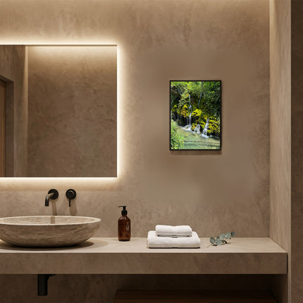 Poster paesaggistico naturalistico con cornice in legno noce appeso sopra il lavabo di un bagno moderno con specchio retroilluminato.